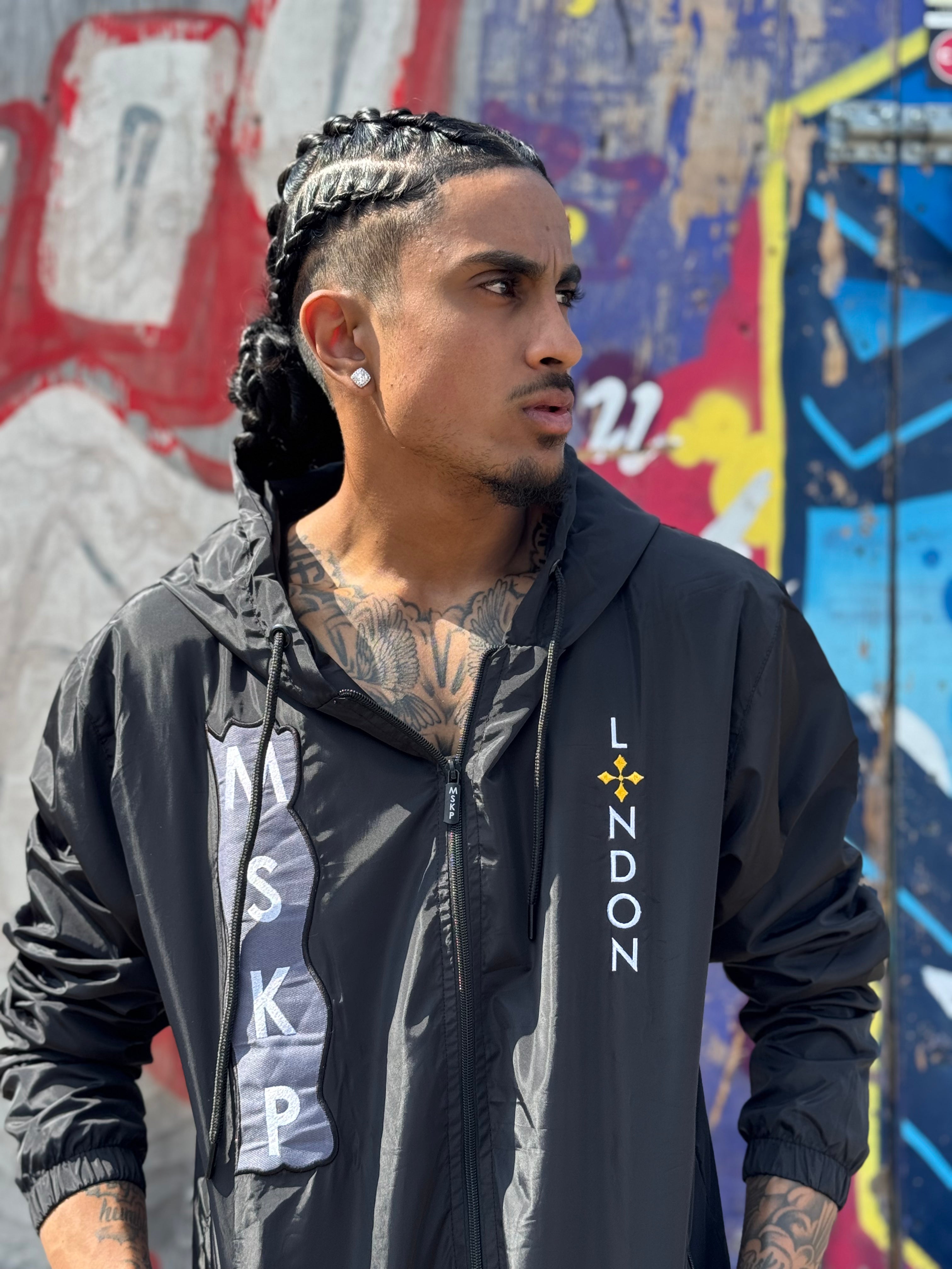 Man wearing a black jacket with 'London' text against a colorful graffiti wall.